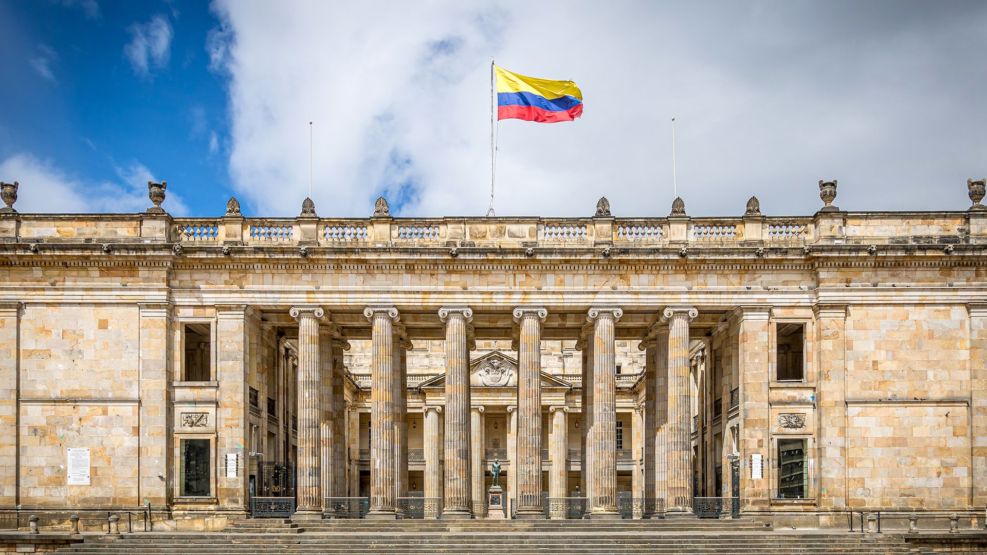 Front of Congress of Colombia building with flag waving on top below the sky